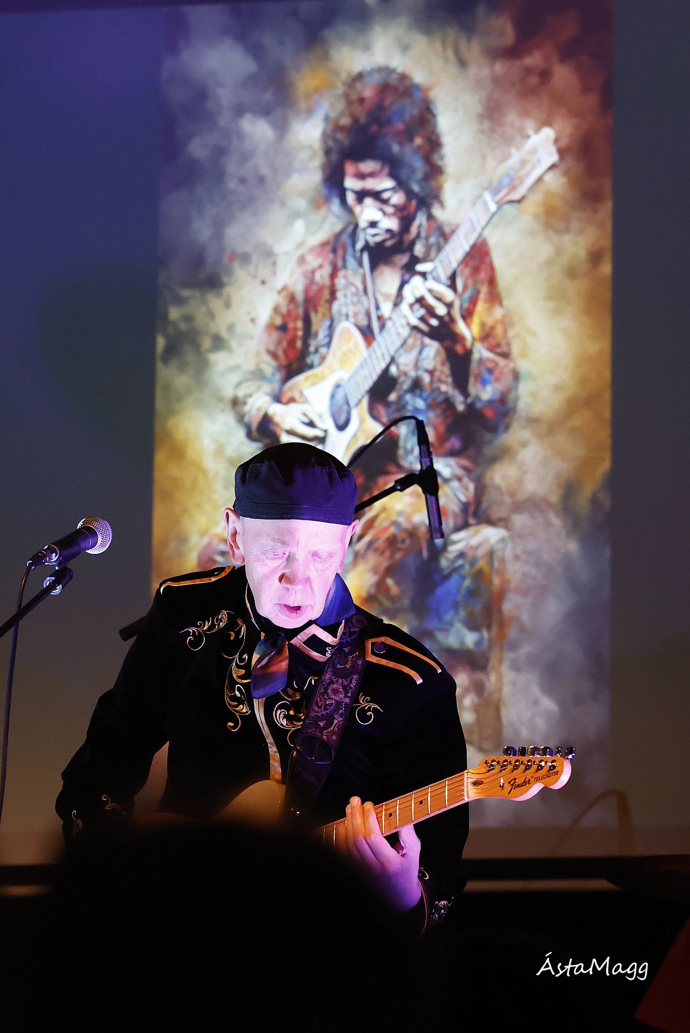 Bjössi Thor í skrautlegum svörtum jakka spilar á rafmagnsgítar fyrir framan sviðsmynd með stórri mynd af Jimy Hendrix